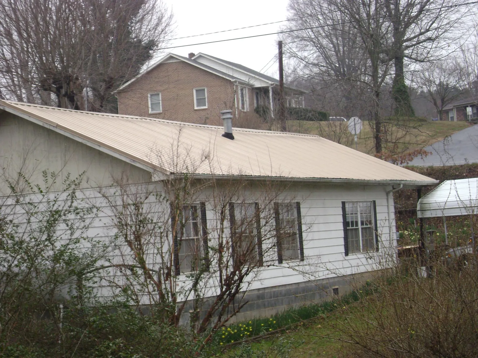 Tan metal roof on a white sided house set into a hillside — Commercial Roofing by Roofing Brothers in Mound City